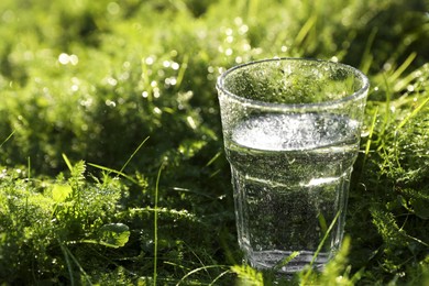 Glass of fresh water on green grass outdoors, closeup. Space for text