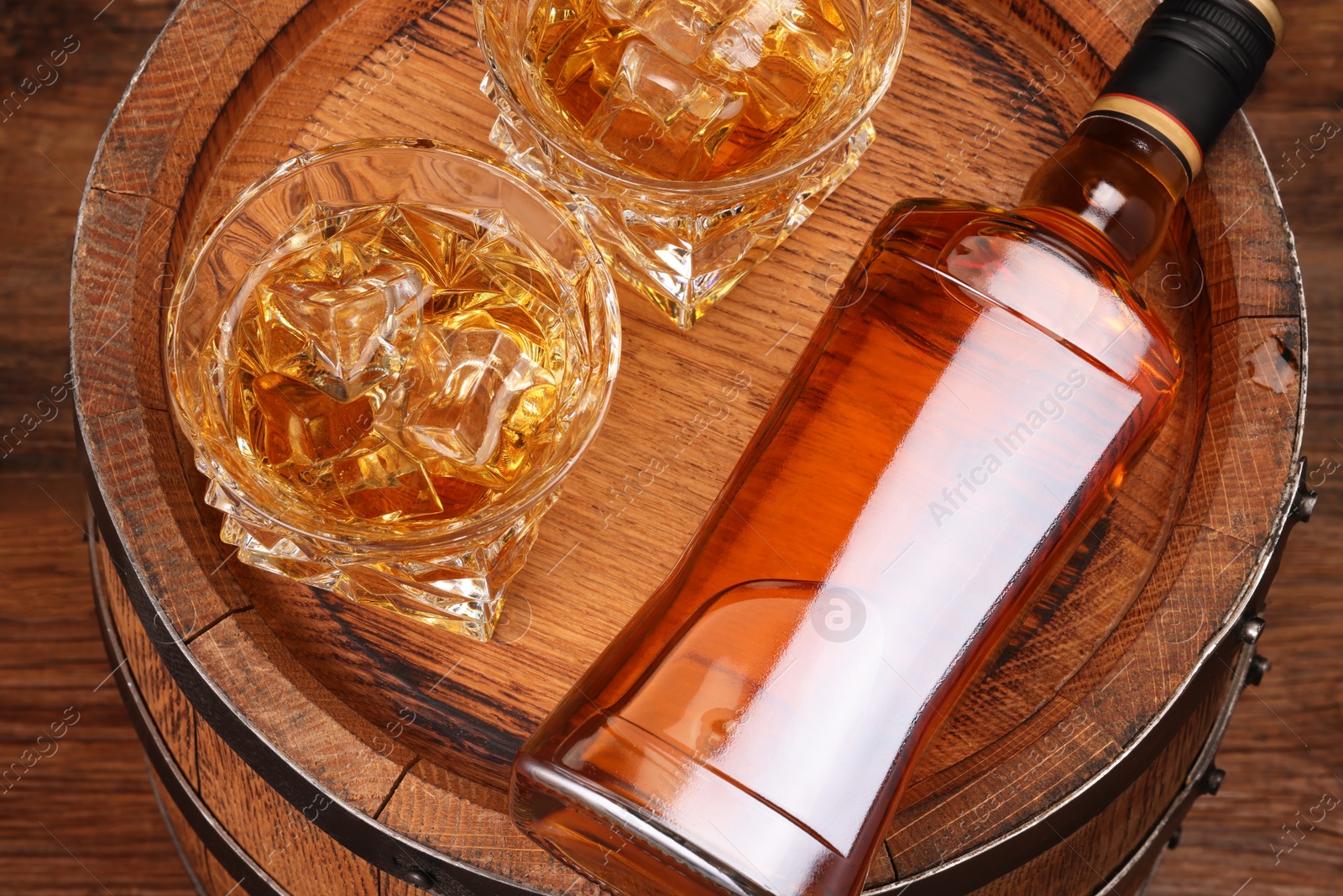 Photo of Whiskey with ice cubes in glasses, bottle and barrel on wooden table, above view