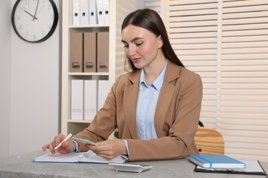 Photo of Happy woman taking notes at light grey marble table in office