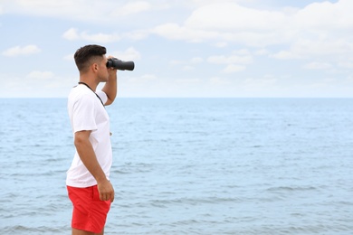 Photo of Handsome male lifeguard with binocular near sea