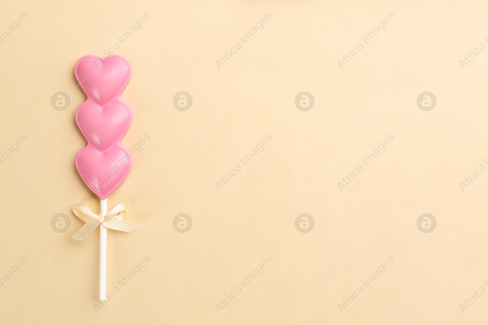 Photo of Chocolate heart shaped lollipop on beige background, top view. Space for text
