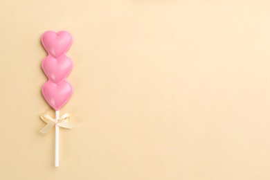 Photo of Chocolate heart shaped lollipop on beige background, top view. Space for text