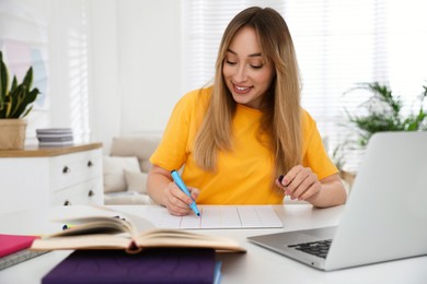 Young woman writing down notes during webinar at table in room
