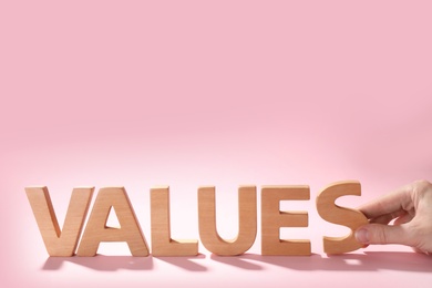 Woman making word VALUES with wooden letters on pink background, closeup