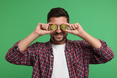 Photo of Man covering his eyes with halves of kiwi on green background