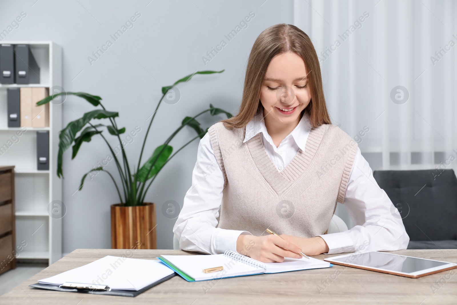 Photo of Woman taking notes at wooden table in office