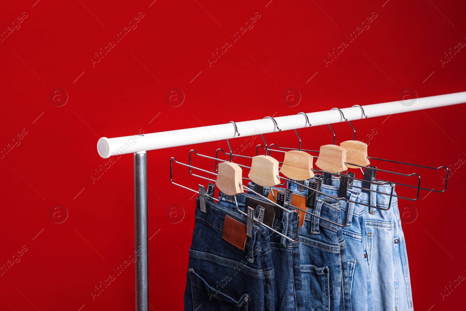 Photo of Rack with different jeans on red background