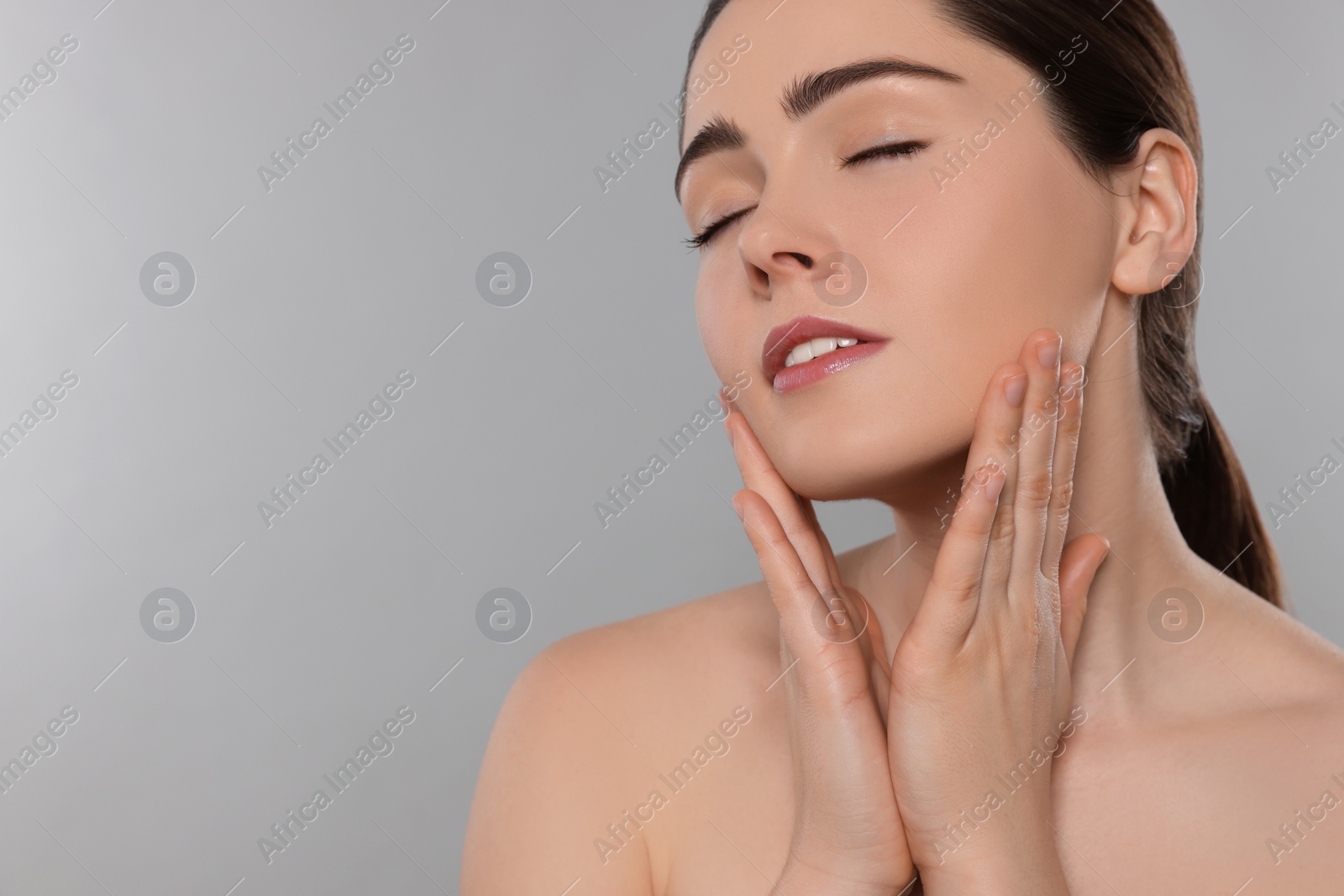 Photo of Young woman massaging her face on grey background. Space for text