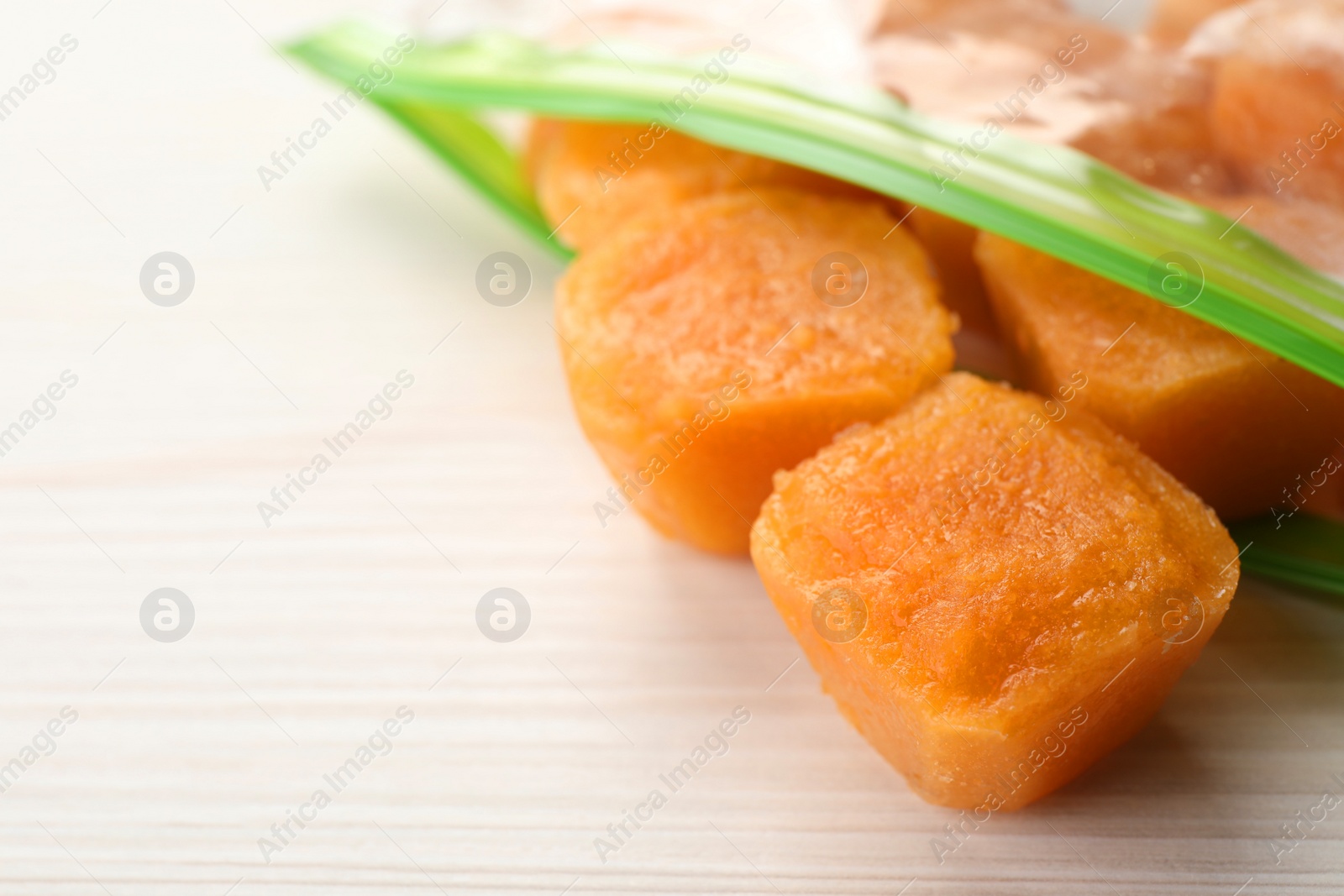 Photo of Frozen nectarine puree cubes in plastic bag on white wooden table, closeup. Space for text