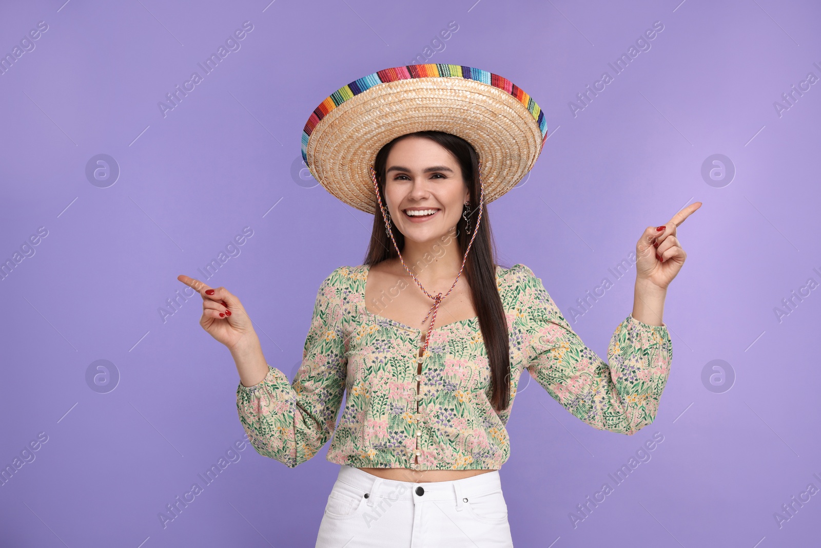 Photo of Young woman in Mexican sombrero hat showing something on violet background