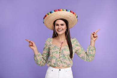 Photo of Young woman in Mexican sombrero hat showing something on violet background