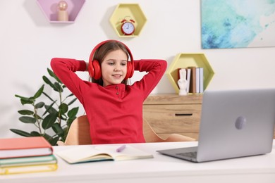 Photo of E-learning. Cute girl using laptop and headphones during online lesson at table indoors