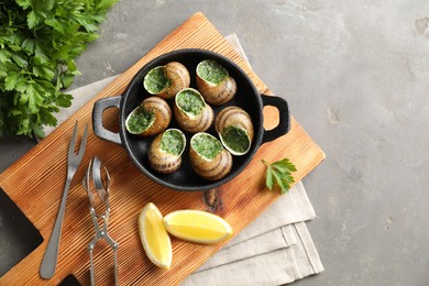 Photo of Delicious cooked snails in baking dish served on grey textured table, flat lay