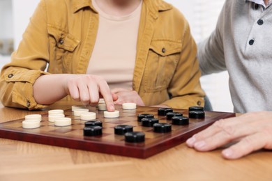 Photo of Playing checkers. Senior man learning woman at table in room, closeup