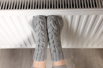 Photo of Woman warming feet near heating radiator, above view