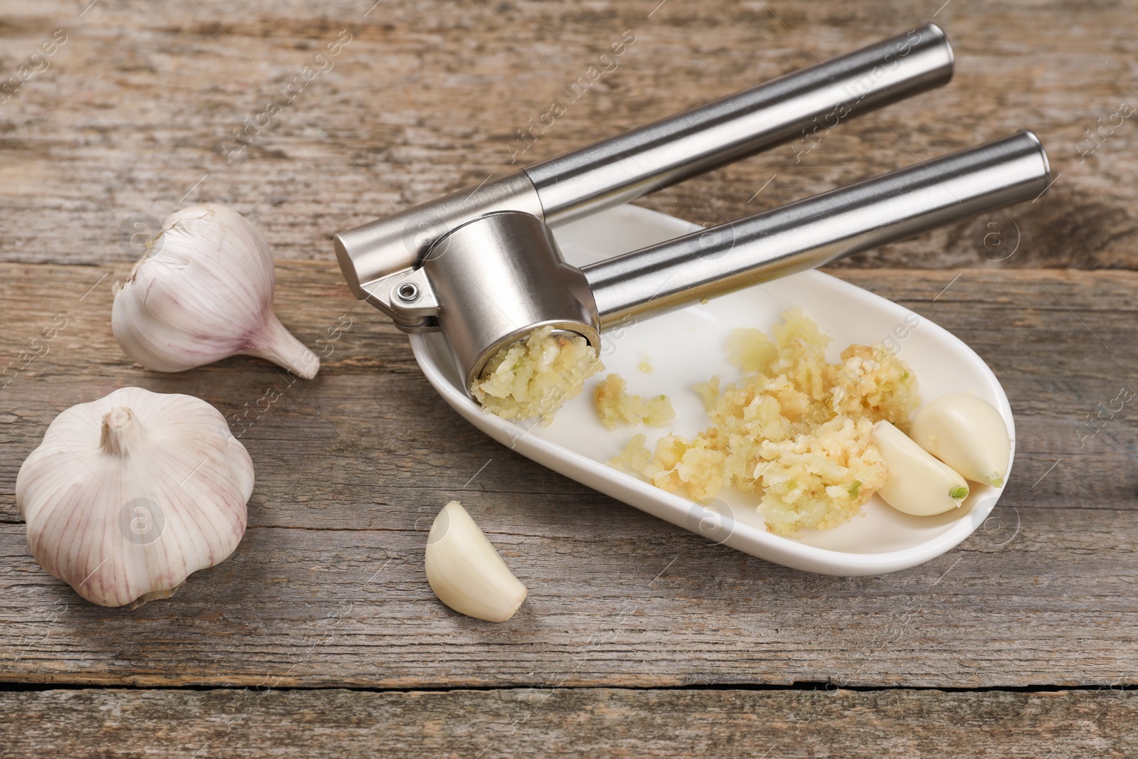 Photo of Garlic press, cloves and mince on wooden table, above view