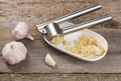 Photo of Garlic press, cloves and mince on wooden table, above view