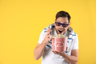 Emotional man with 3D glasses and tasty popcorn on color background. Space for text