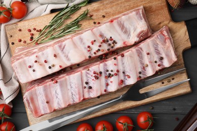 Photo of Raw pork ribs with peppercorns, rosemary and tomatoes on grey wooden table, flat lay