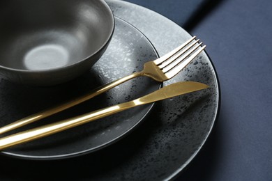 Stylish ceramic plates, bowl and cutlery on dark blue background, closeup