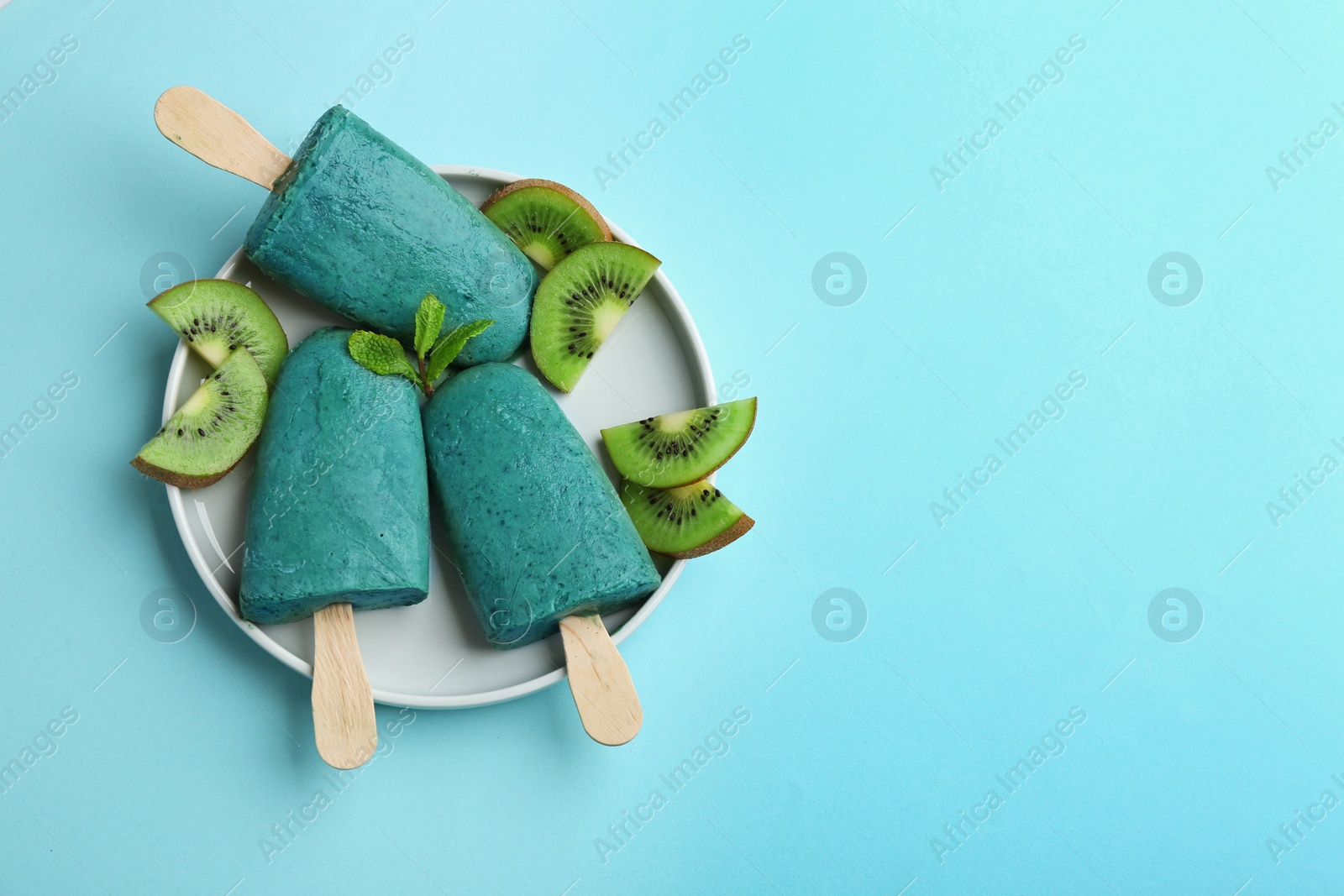 Photo of Plate with delicious spirulina popsicles and kiwi on color background, top view. Space for text