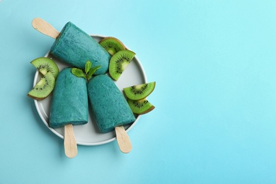 Photo of Plate with delicious spirulina popsicles and kiwi on color background, top view. Space for text