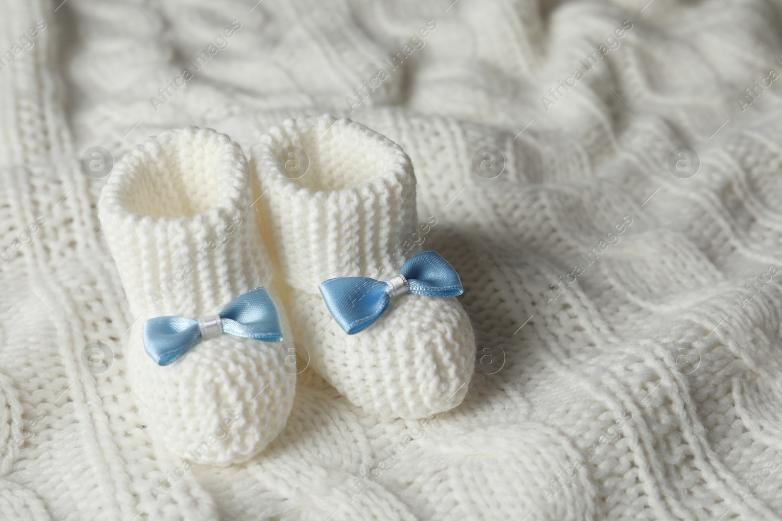 Photo of Handmade baby booties on soft plaid. Space for text