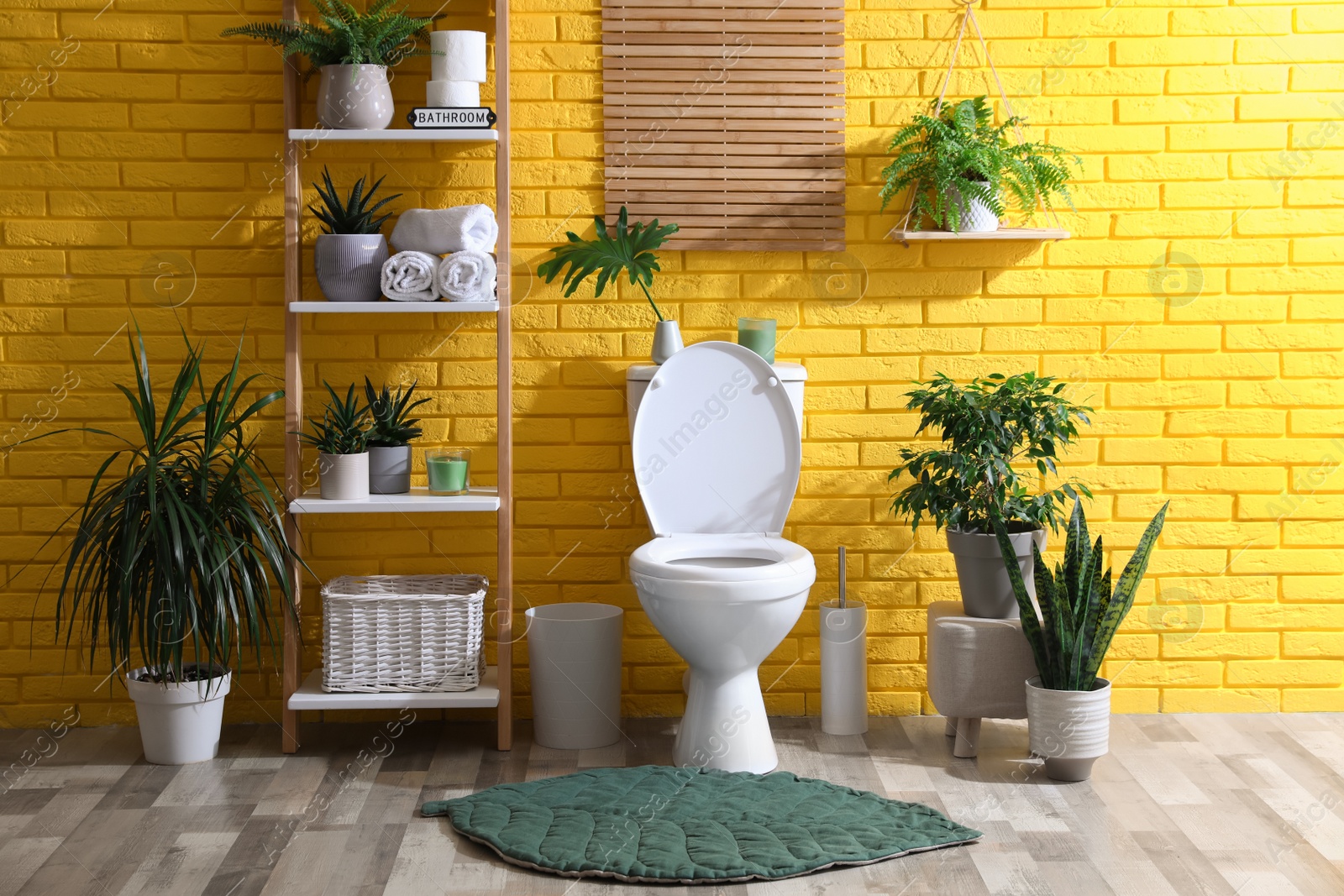 Photo of Stylish bathroom with toilet bowl and green plants near yellow brick wall. Interior design