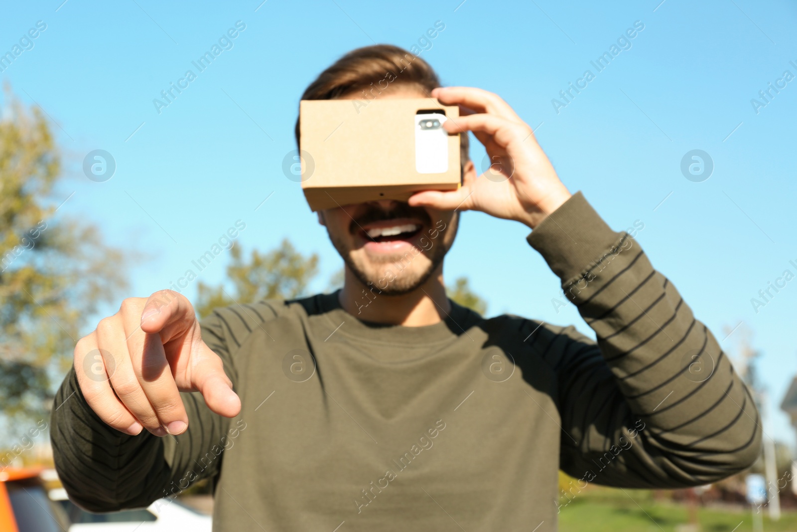 Photo of Young man using cardboard virtual reality headset outdoors