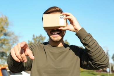 Young man using cardboard virtual reality headset outdoors