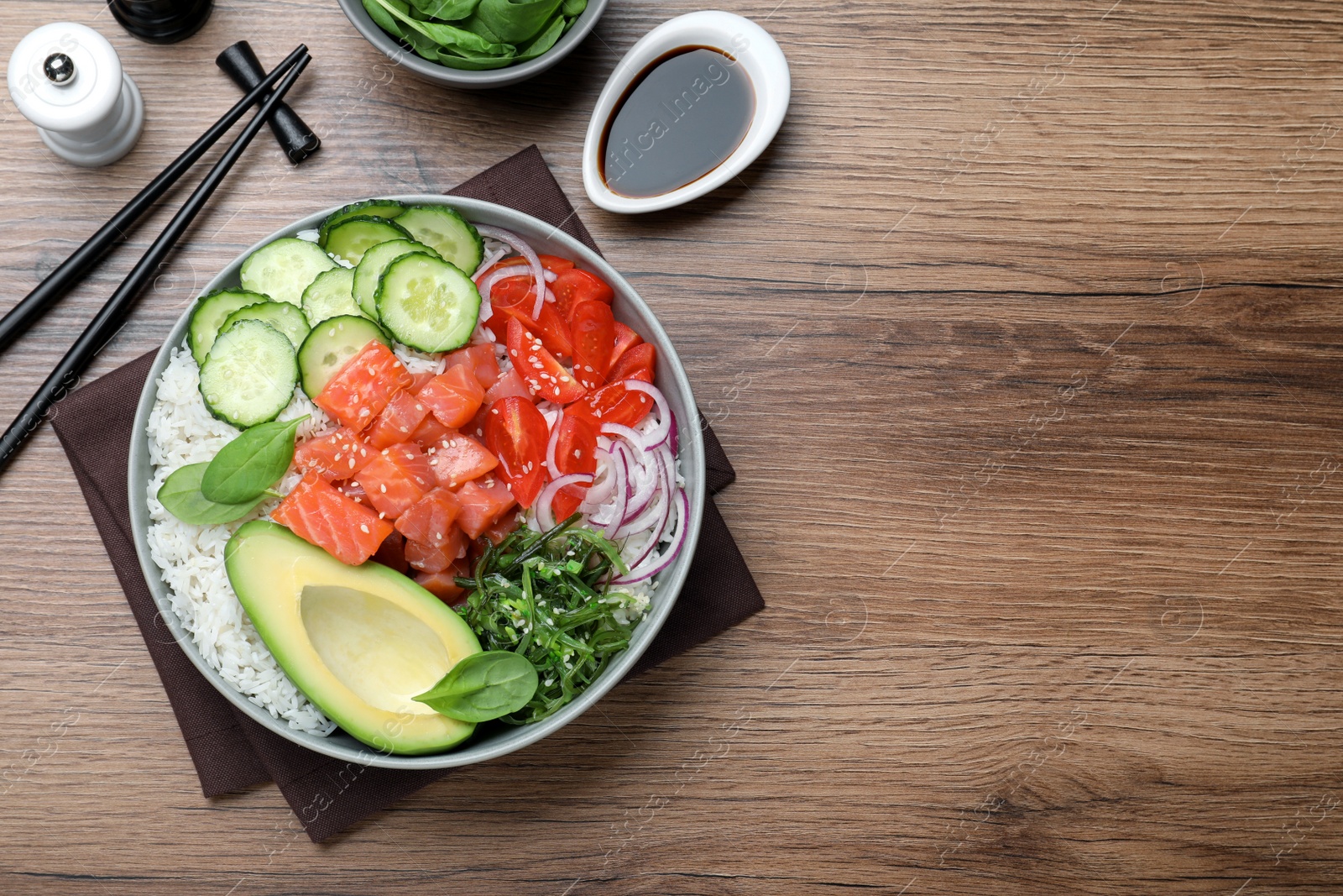 Photo of Delicious poke bowl with salmon and vegetables served on wooden table, flat lay. space for text