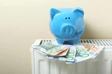 Piggy bank and euro banknotes on heating radiator near beige wall