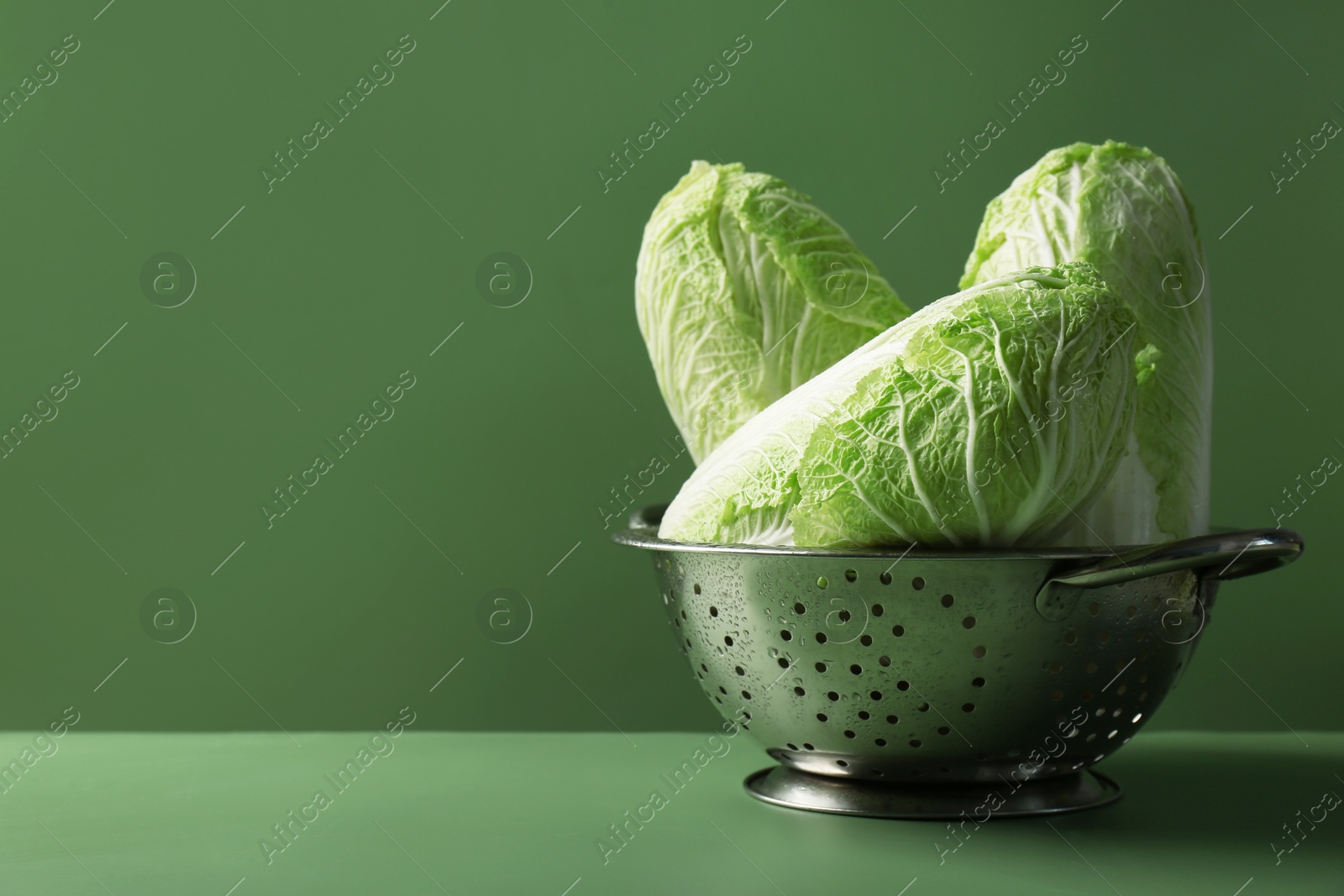 Photo of Fresh Chinese cabbages in colander on green background, closeup. Space for text