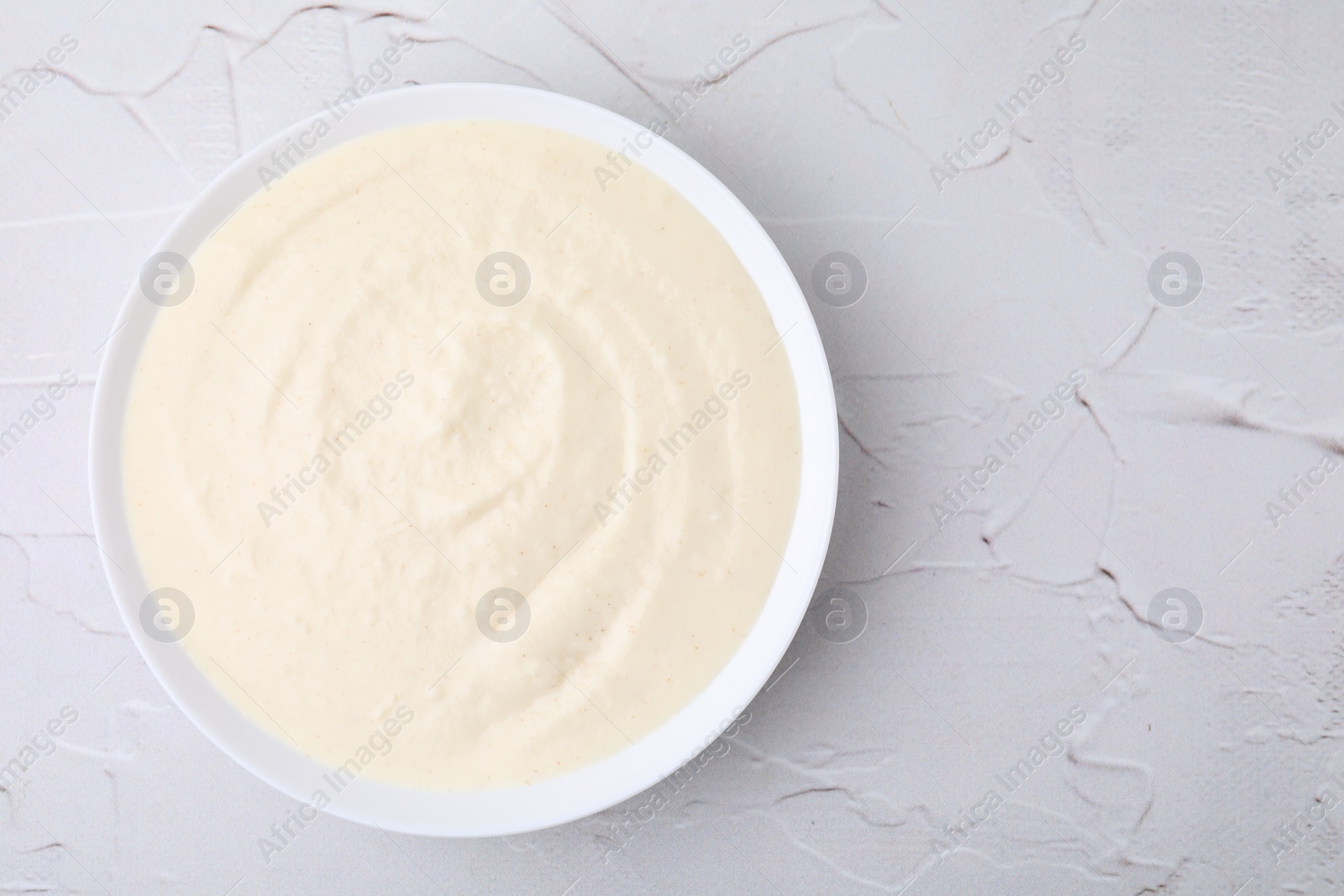 Photo of Delicious semolina pudding in bowl on white textured table, top view. Space for text