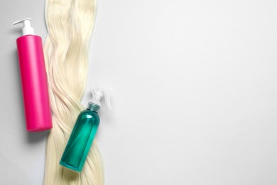Photo of Spray bottles with thermal protection and lock of blonde hair on light background, flat lay. Space for text
