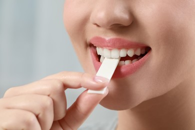 Photo of Woman putting chewing gum piece into mouth on blurred background, closeup