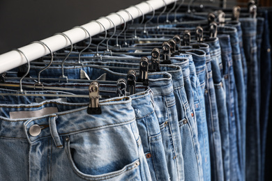 Rack with different jeans on dark grey background, closeup