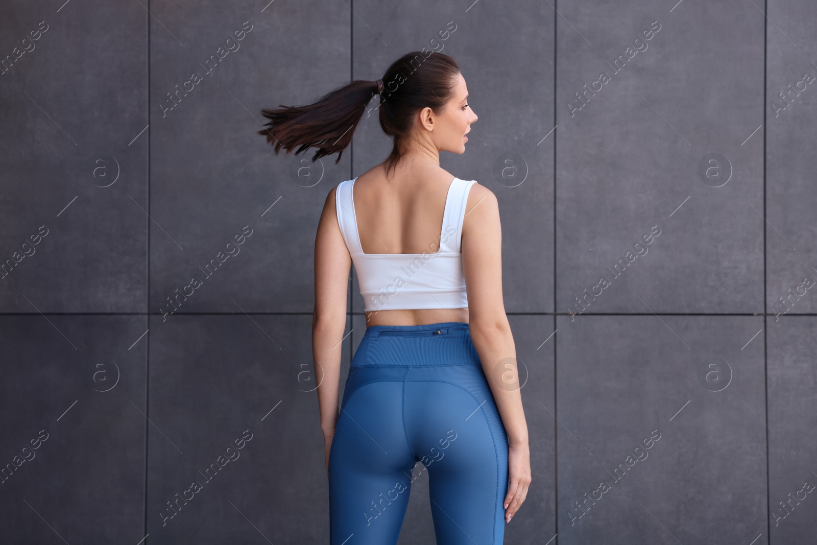 Photo of Woman in sportswear near dark grey wall, back view