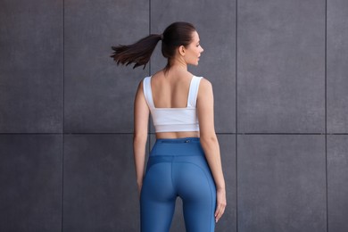 Woman in sportswear near dark grey wall, back view