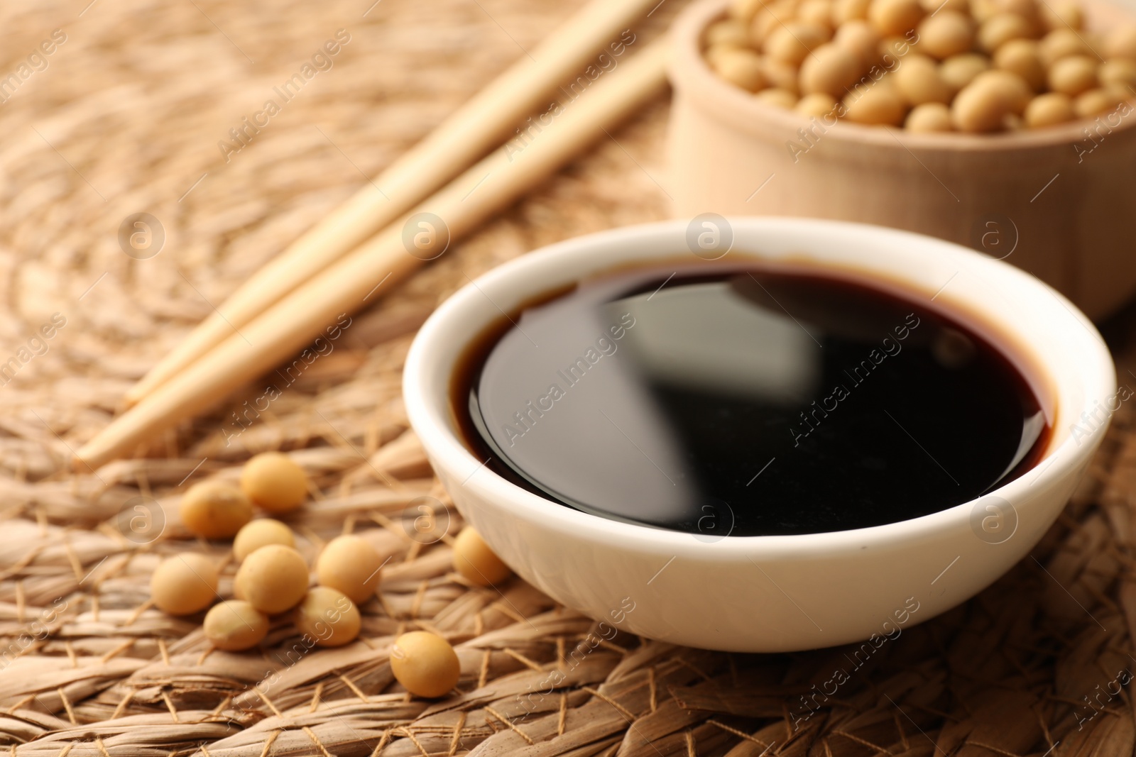 Photo of Soy sauce in bowl and soybeans on wicker mat, closeup