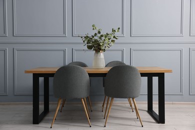 Photo of Soft chairs, table and vase with eucalyptus branches in stylish dining room