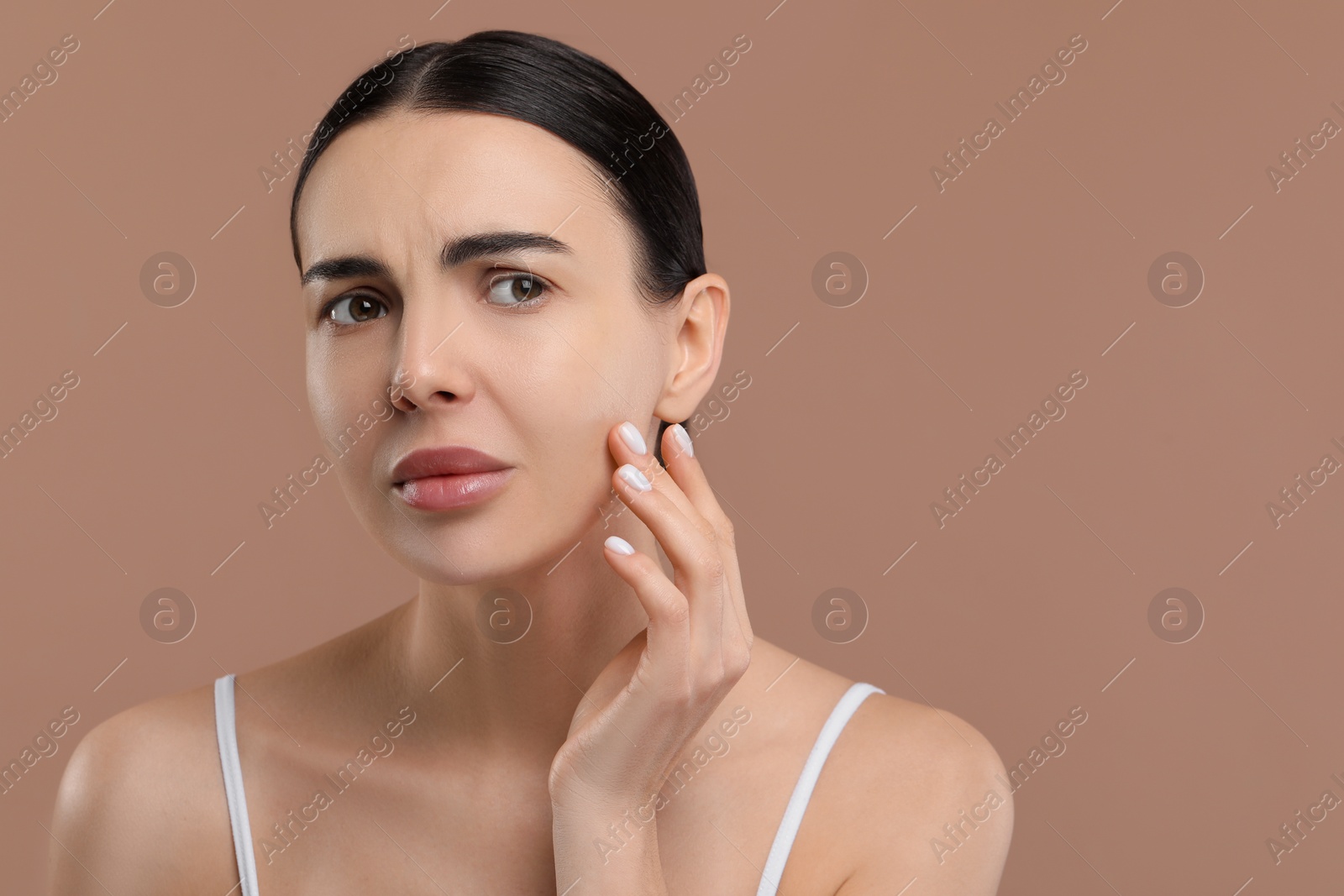 Photo of Woman with dry skin checking her face on beige background, space for text