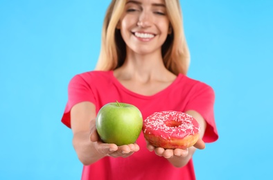 Photo of Woman choosing between doughnut and healthy apple on light blue background, focus on hands