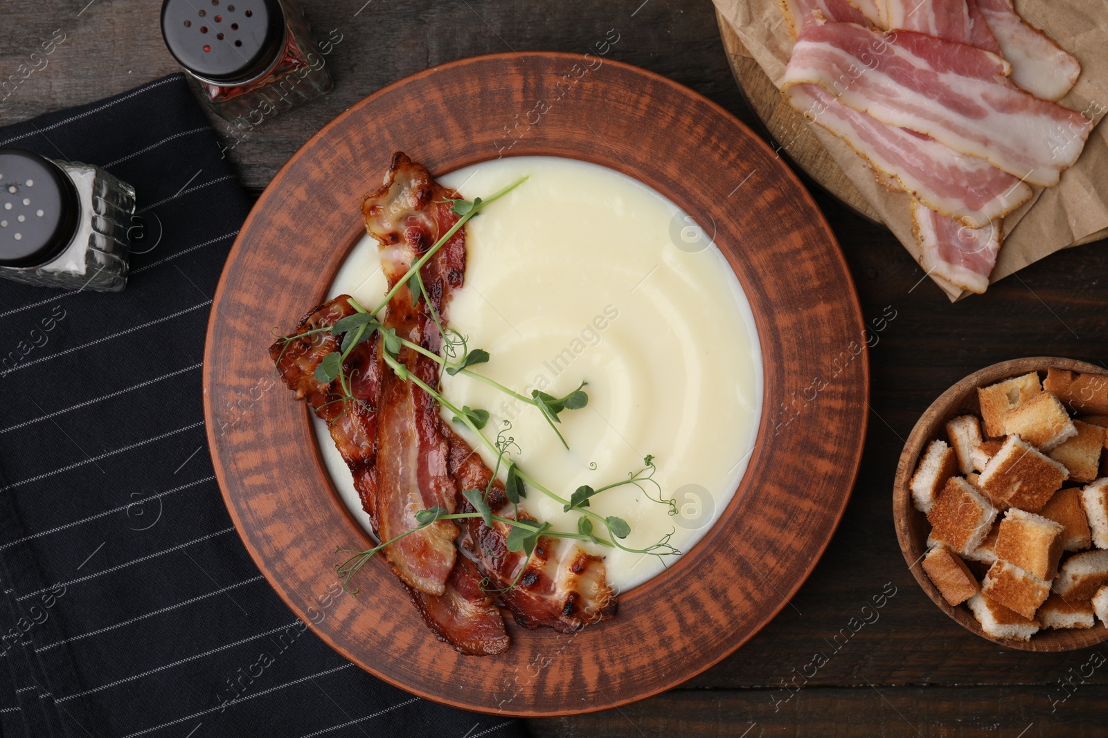 Photo of Delicious potato soup with bacon and microgreens in bowl on wooden table, flat lay