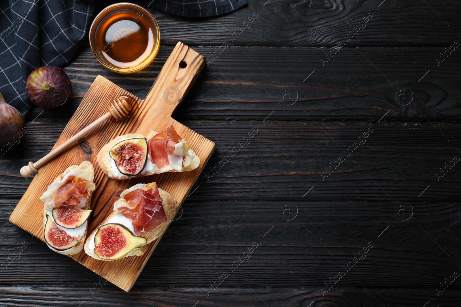Photo of Sandwiches with ripe figs, prosciutto and cream cheese served on black wooden table, flat lay. Space for text