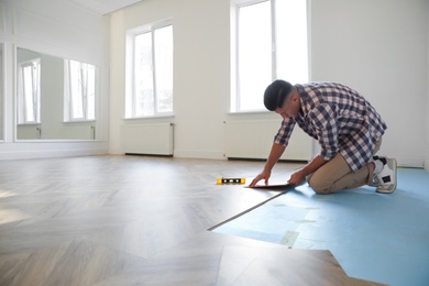 Photo of Professional worker installing new parquet flooring indoors