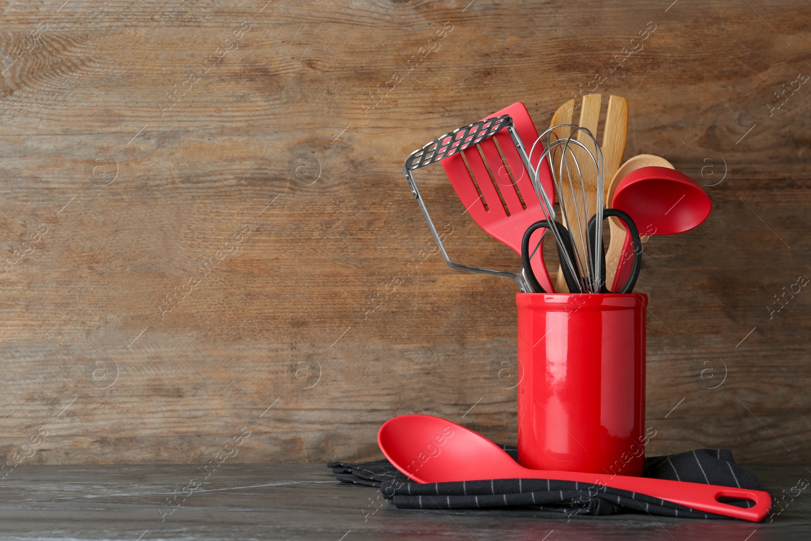 Photo of Holder with kitchen utensils on table against wooden background. Space for text