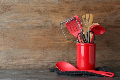 Photo of Holder with kitchen utensils on table against wooden background. Space for text