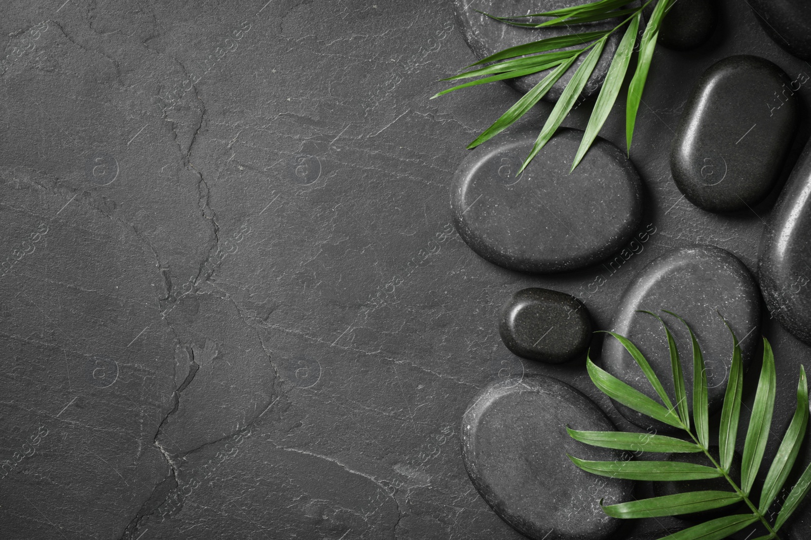 Photo of Spa stones and green leaves on black table. Space for text