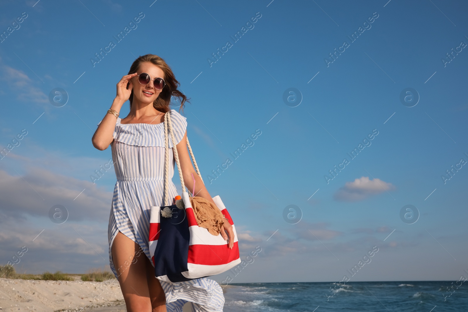 Photo of Beautiful woman with beach bag walking on sand near sea